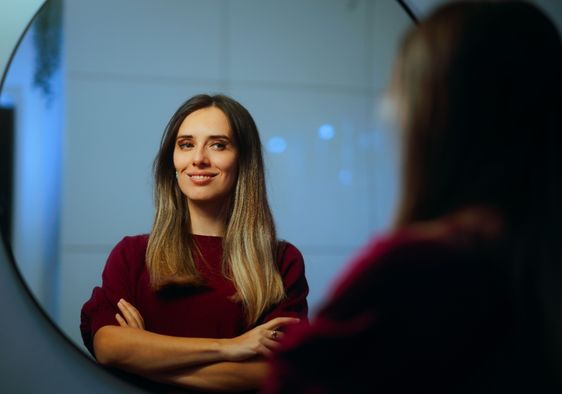 A happy woman smiles while she looks at herself in the mirror.