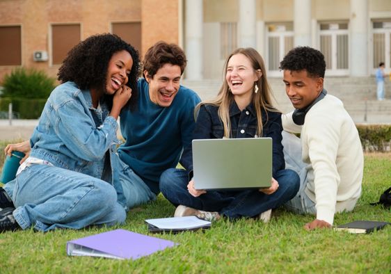 A diverse group of young adults sitting on the grass and smiling.