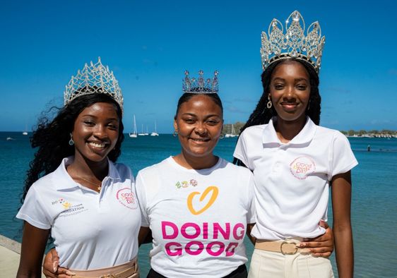Three women wearing tiaras and Good Deeds Day shirts stand by the water.