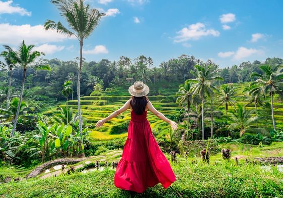 A female tourist in a red dress looks at a rice terrace in Bali, Indonesia.