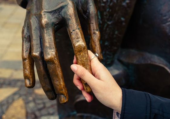 A visually impaired woman feels the hand of a bronze sculpture.