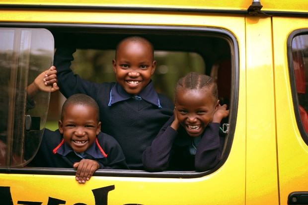 Three School of St Jude students saying hello from a school bus.