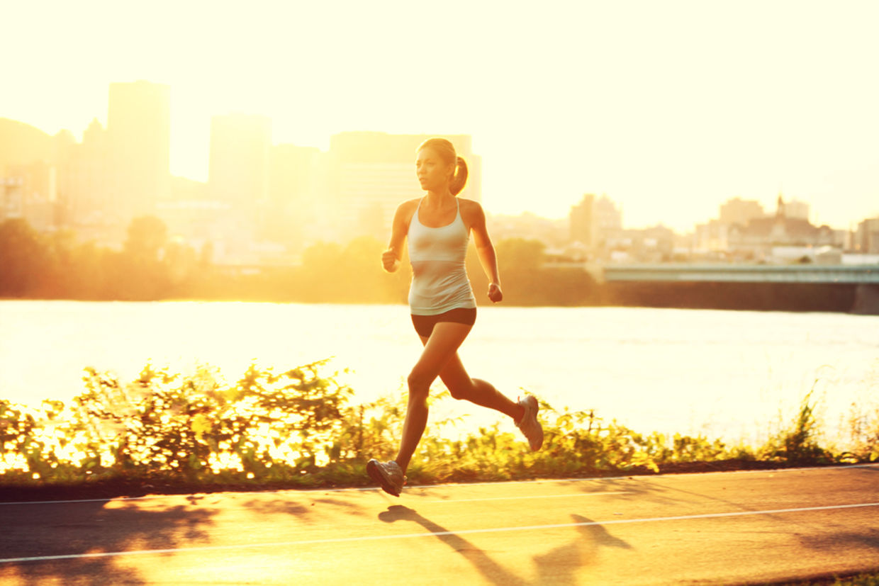female runner running at sunset in city park.