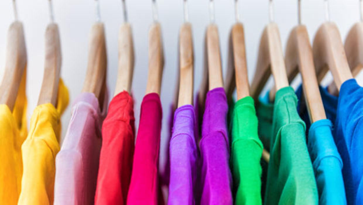 Shirts in different colors hang in a closet.