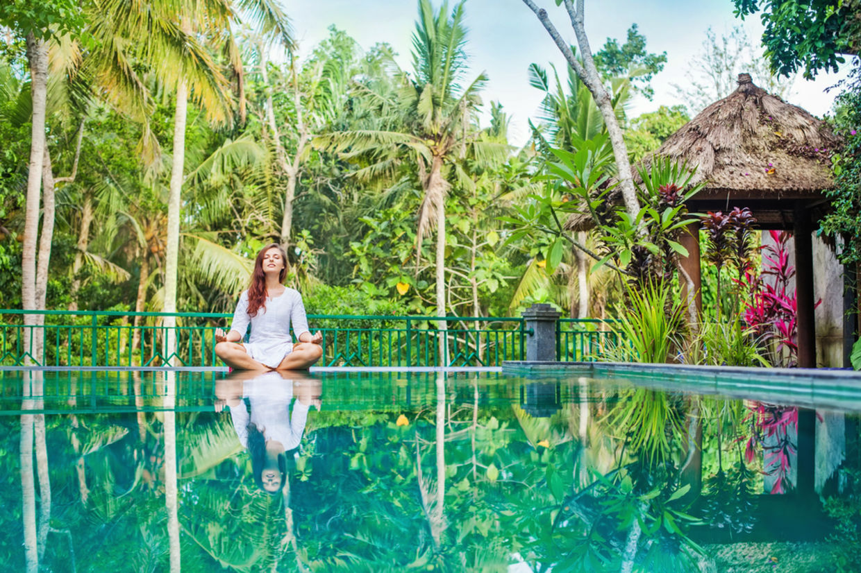 Woman meditation at gorgeous pool side of luxury tropical villa