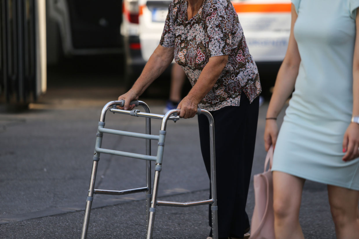 An older woman walks with the help of a walker