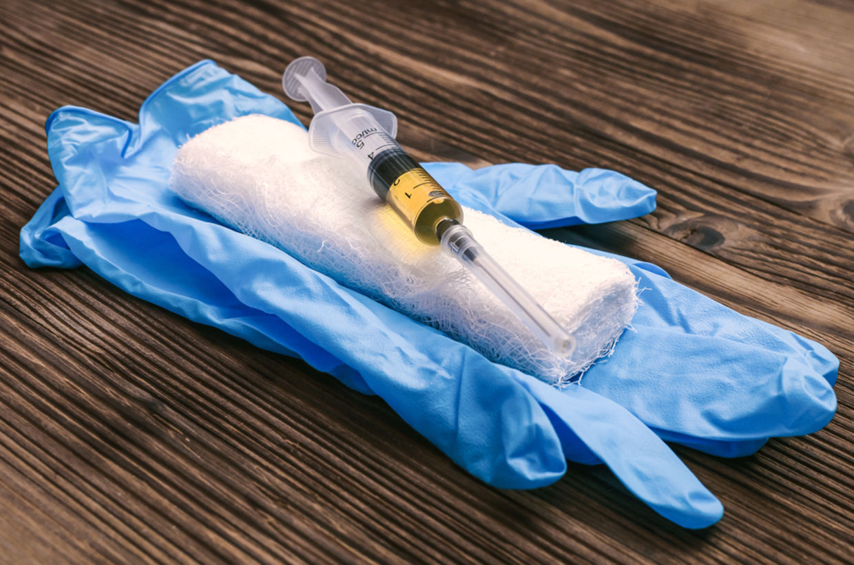 Syringe with orange drug medicine, medicinal gloves and bandage on the doctor table background