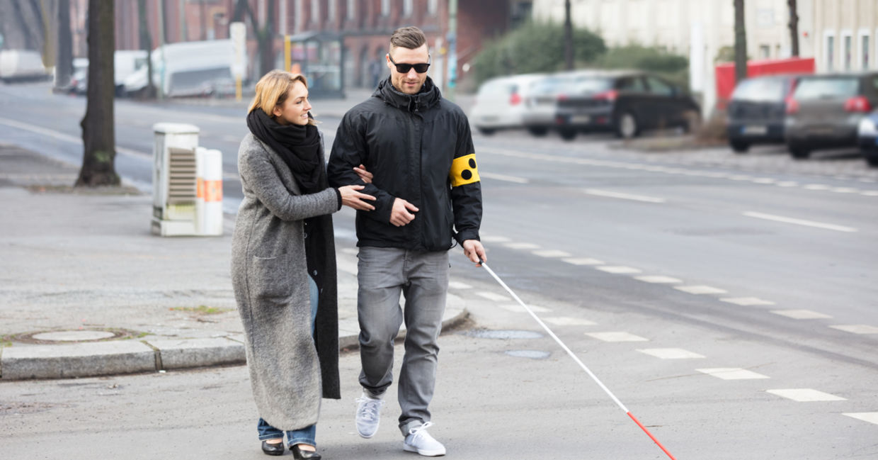 A woman helps a man cross the street