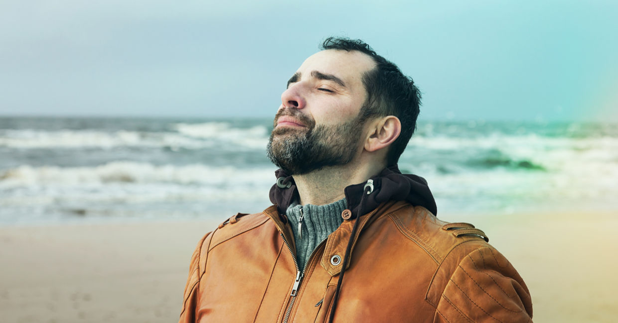 A man on the beach doing deep breathing exercises.