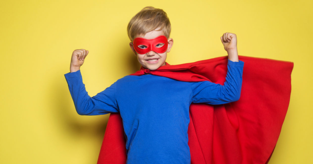 A young boy wearing a superhero mask and cape flexes his muscles and feels strong.