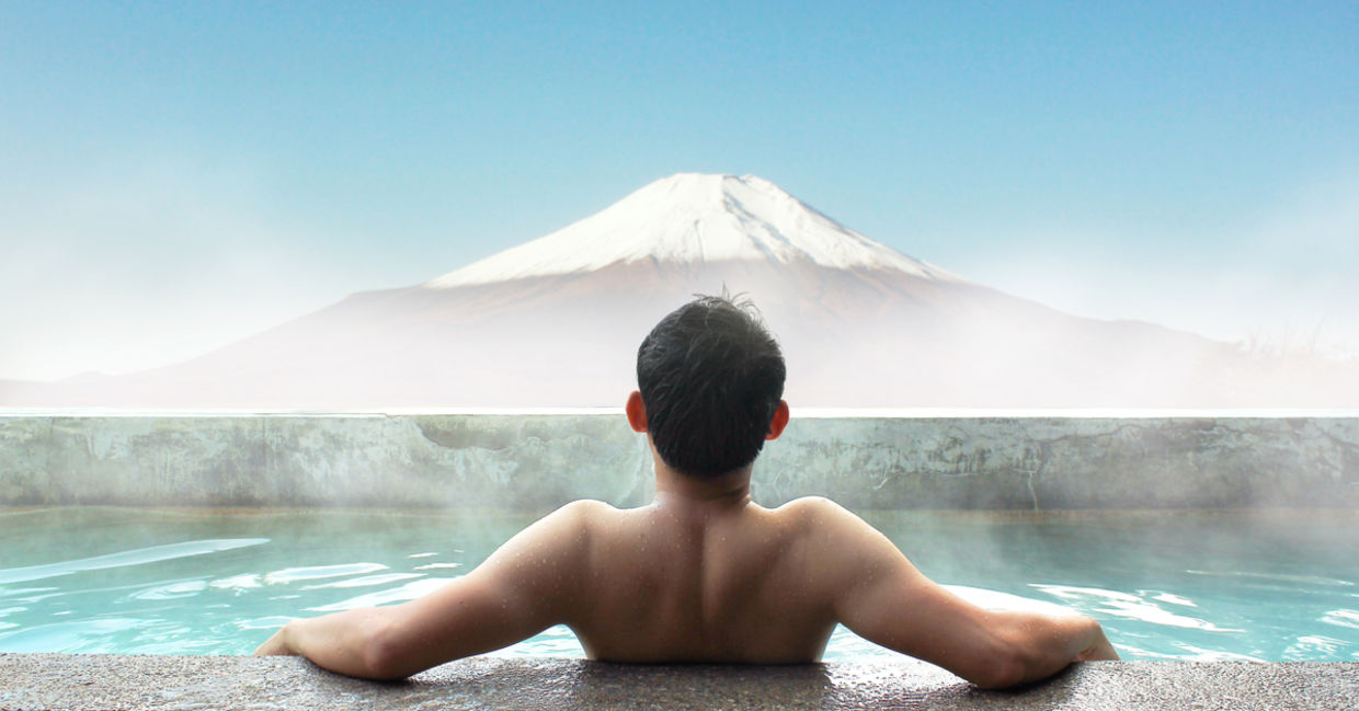 A Japanese man soaking in a hot spring gazes out at Mt. Fuji.