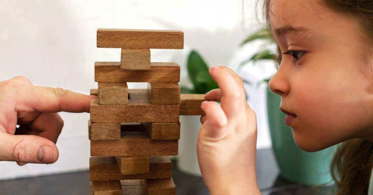 As a father and daughter play tumble tower, dad models resilience by assisting her in strengthening the tower.