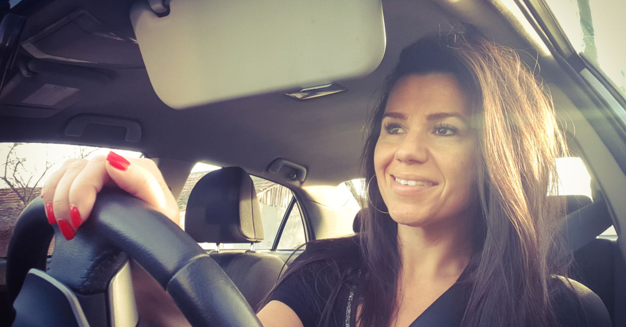 A woman smiling from her car in traffic.