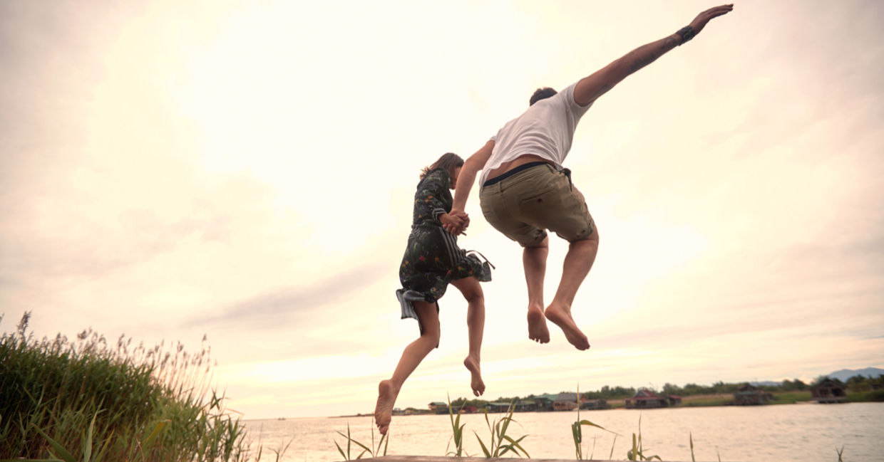 A young couple spontaneously jumps into a river.