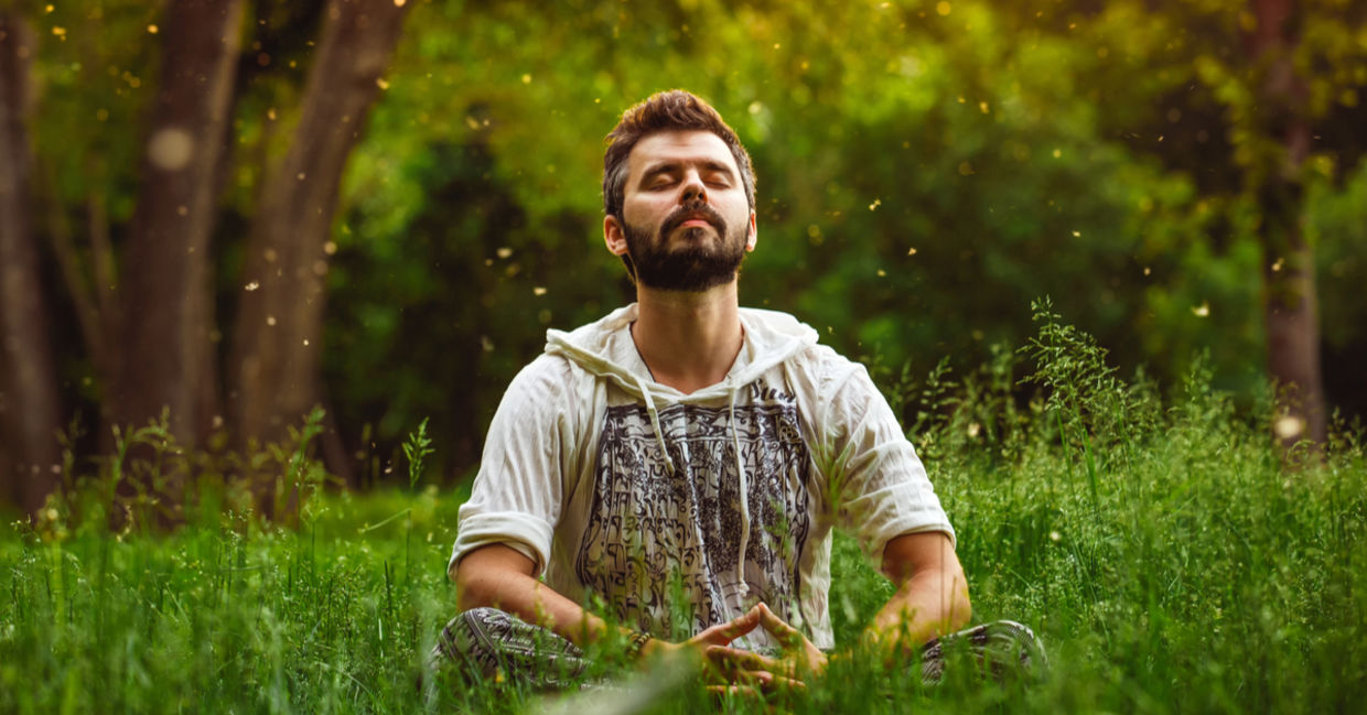 A young man meditates in a sunny meadow.