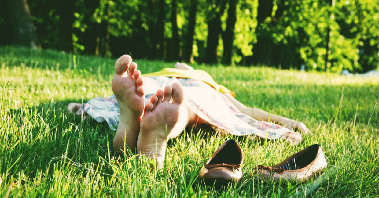 A woman sleeping barefoot on the grass.