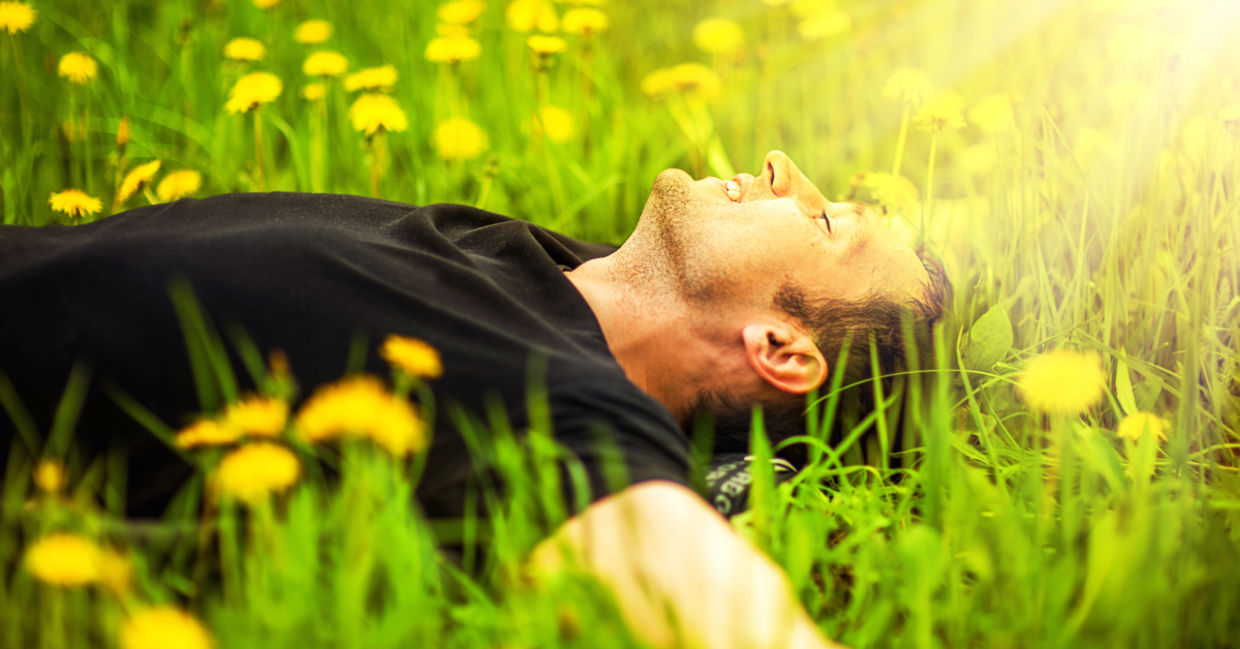 A man lies in a meadow of dandelions, with the sun shining on his smiling face.