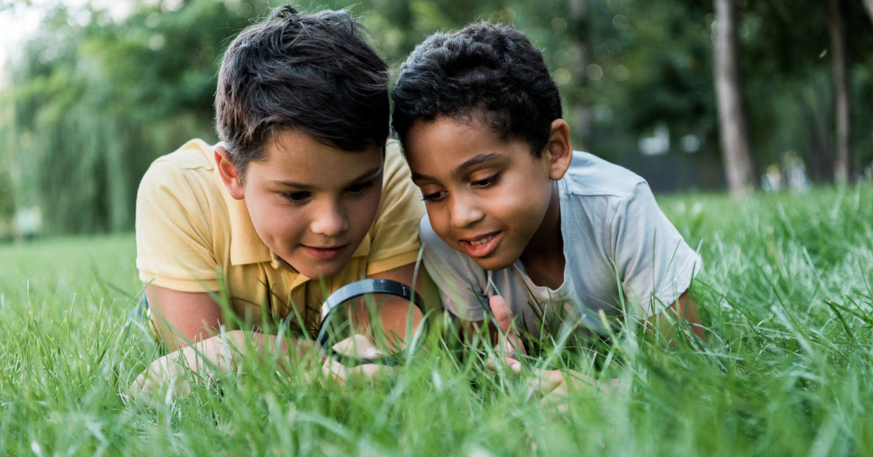 Boys looking at grass with magnifying glass.