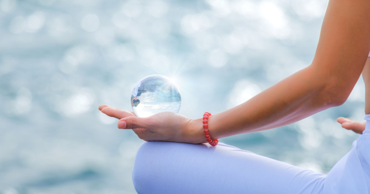 A woman meditates while holding a crystal sphere in her palm.