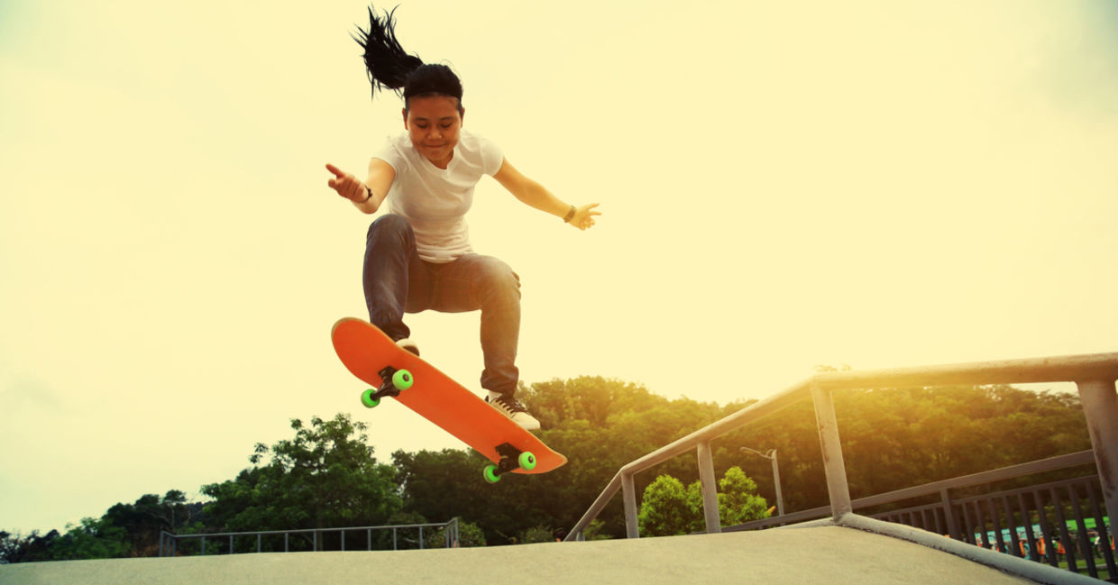 A smiling young girl does an ollie move at a skateboard park.