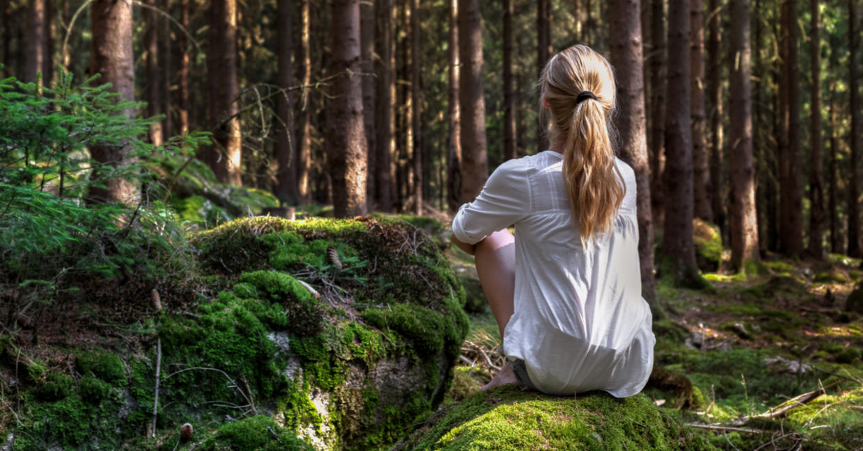 A woman sits on a moss-covered rock enjoying solitude in the forest.