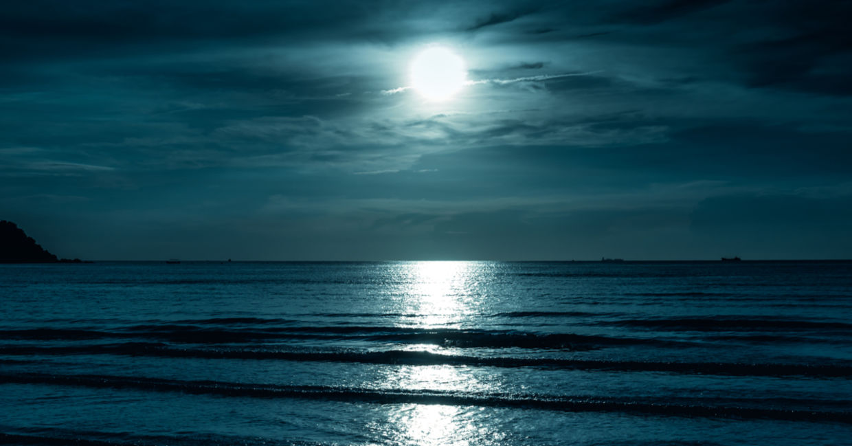 A full moon shines across the sea, creating a reflection on the water that looks like a road.