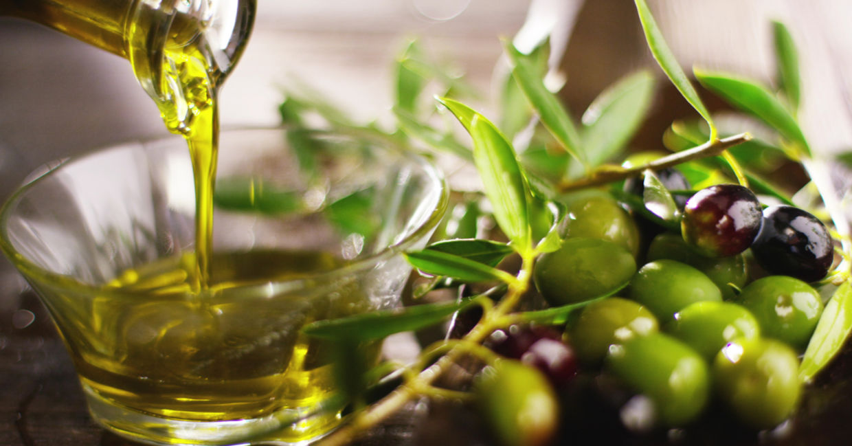Pouring cold pressed olive oil into a bowl beside a branch of olives.