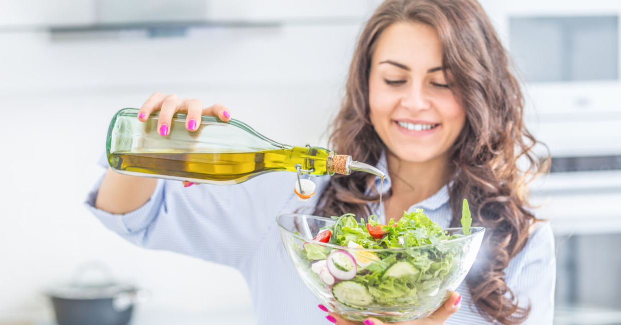 A woman pours olive oil onto a salad.