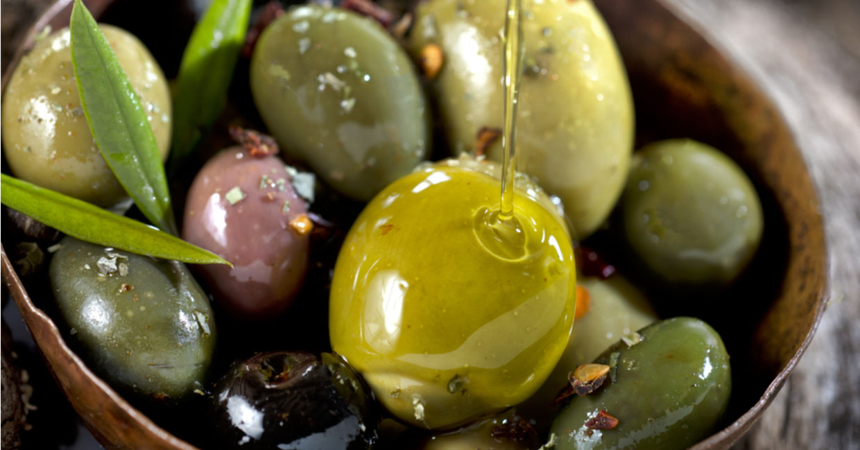 A wooden bowl filled with shiny olives.
