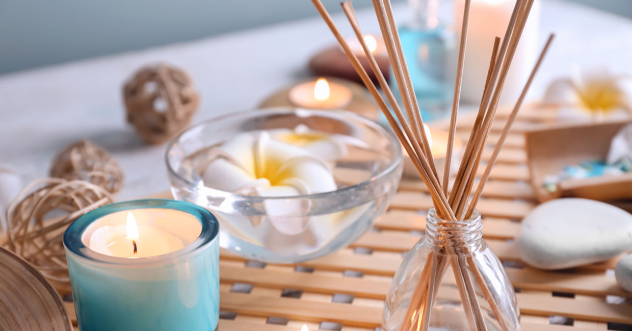 Diffuser reeds in a bottle beside tea lights and flowers.