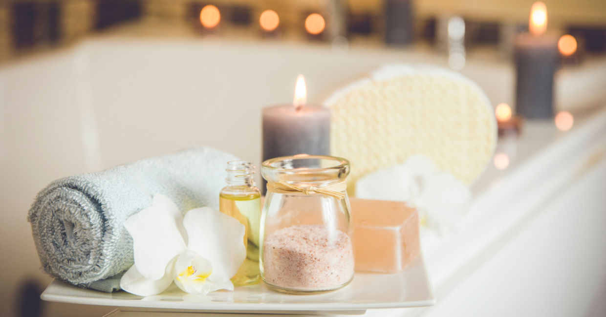 Home spa with rolled towel, bath oil, and candles.
