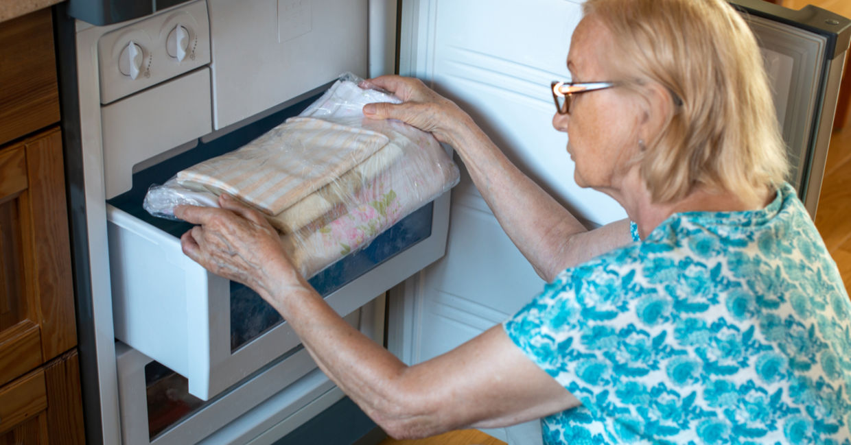 Woman putting bed clothes in the fridge freezer to stay cool in hot weather