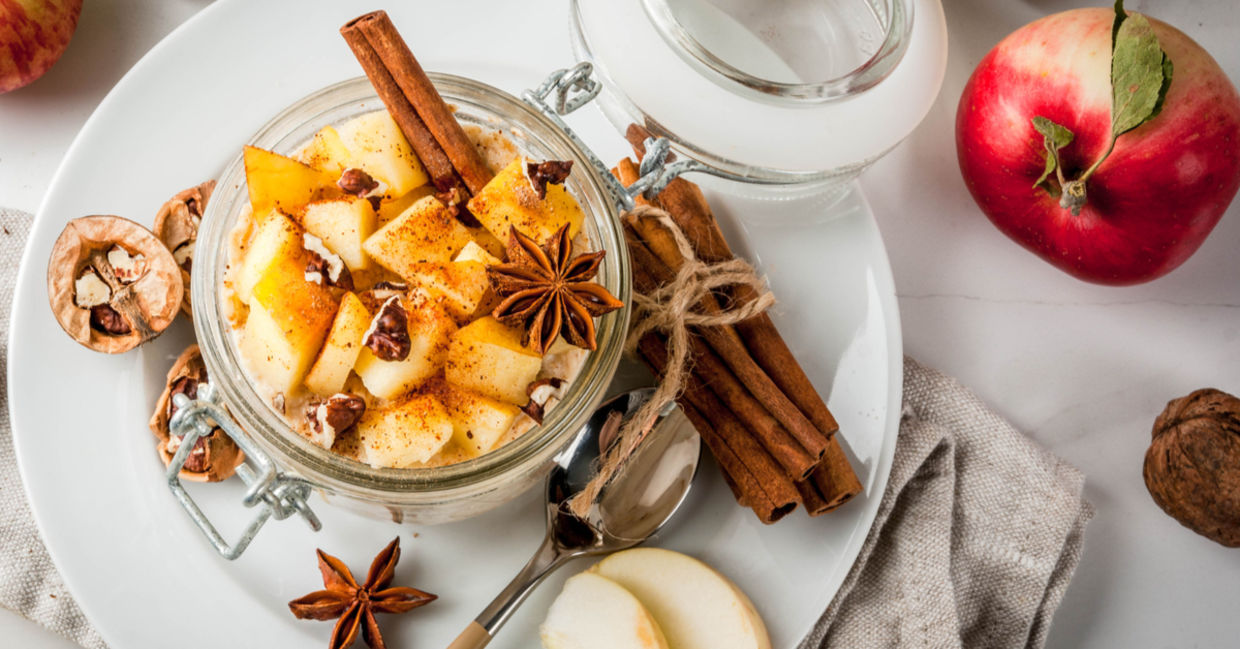 Apple pie overnight oats in a glass jar with cinnamon stick and walnuts.