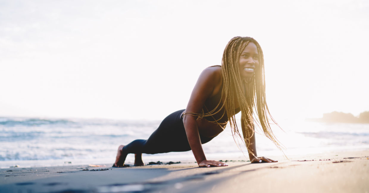 A smiling woman does the plank pose on the sand.