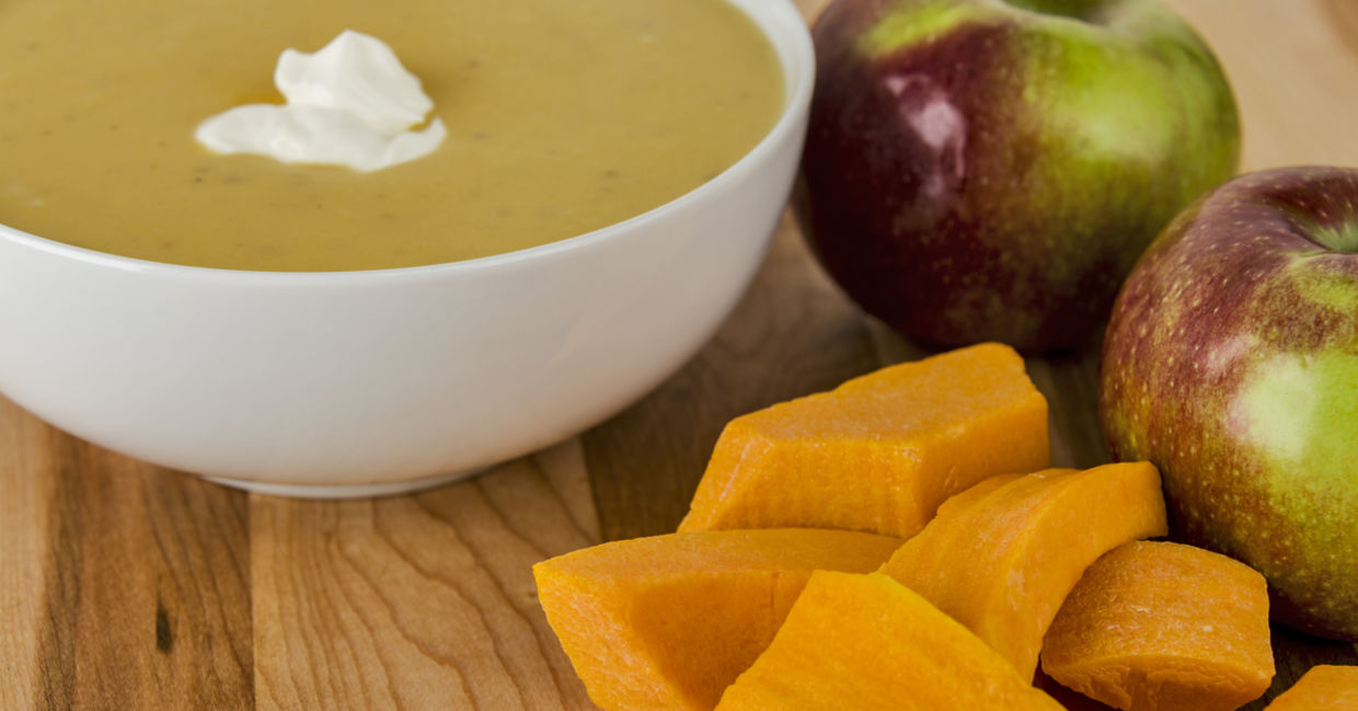 A bowl of butternut squash apple soup with McIntosh apples on the side.