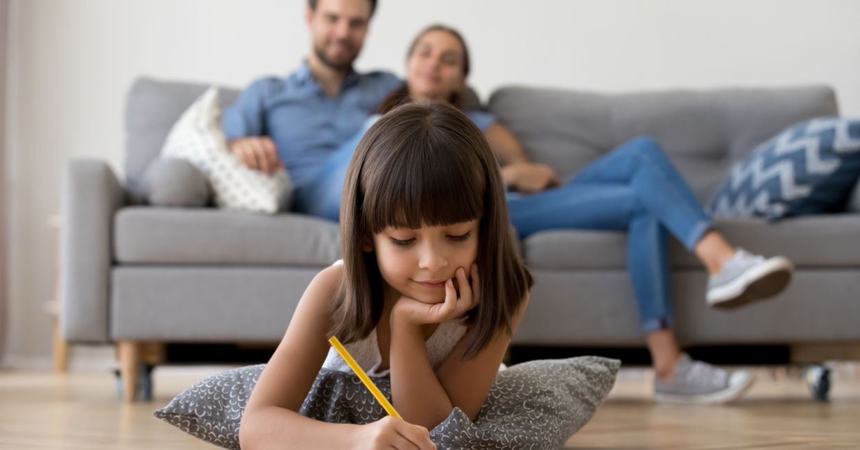 Cute kid drawing while her parents watch her from the sofa