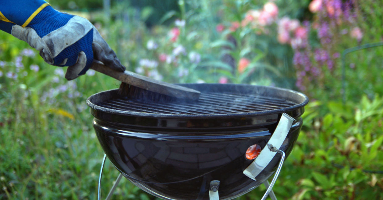 A man uses a grill brush to clean his barbecue.