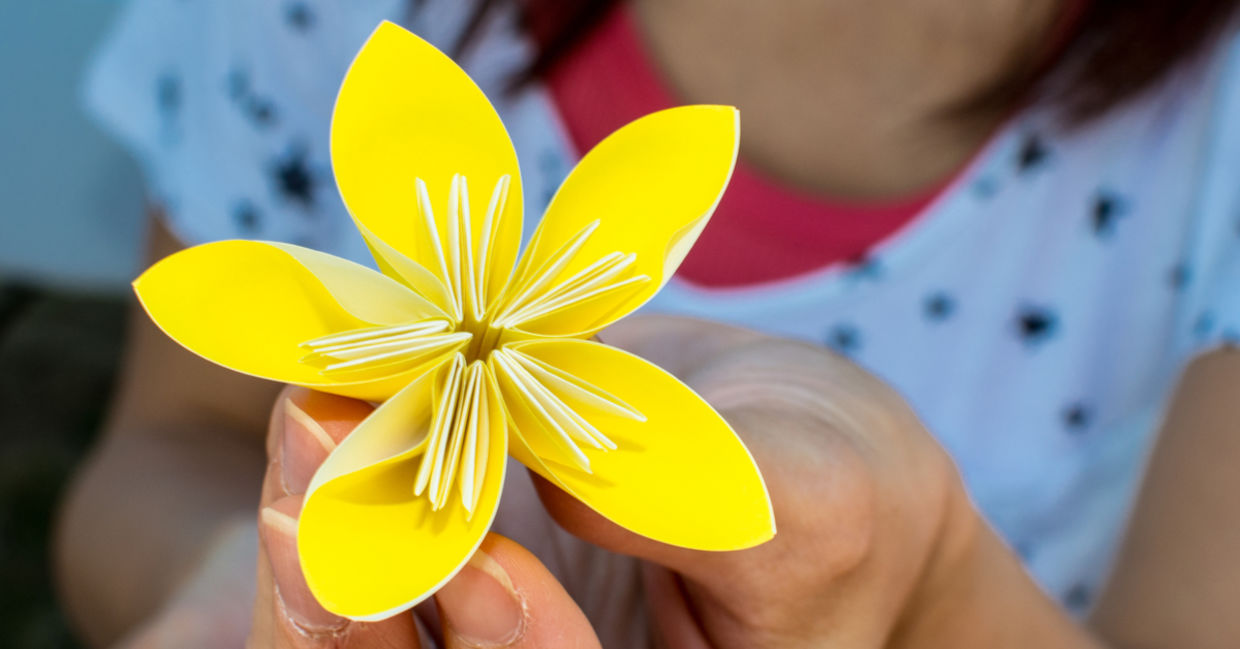 A girl holds a yellow origami flower.