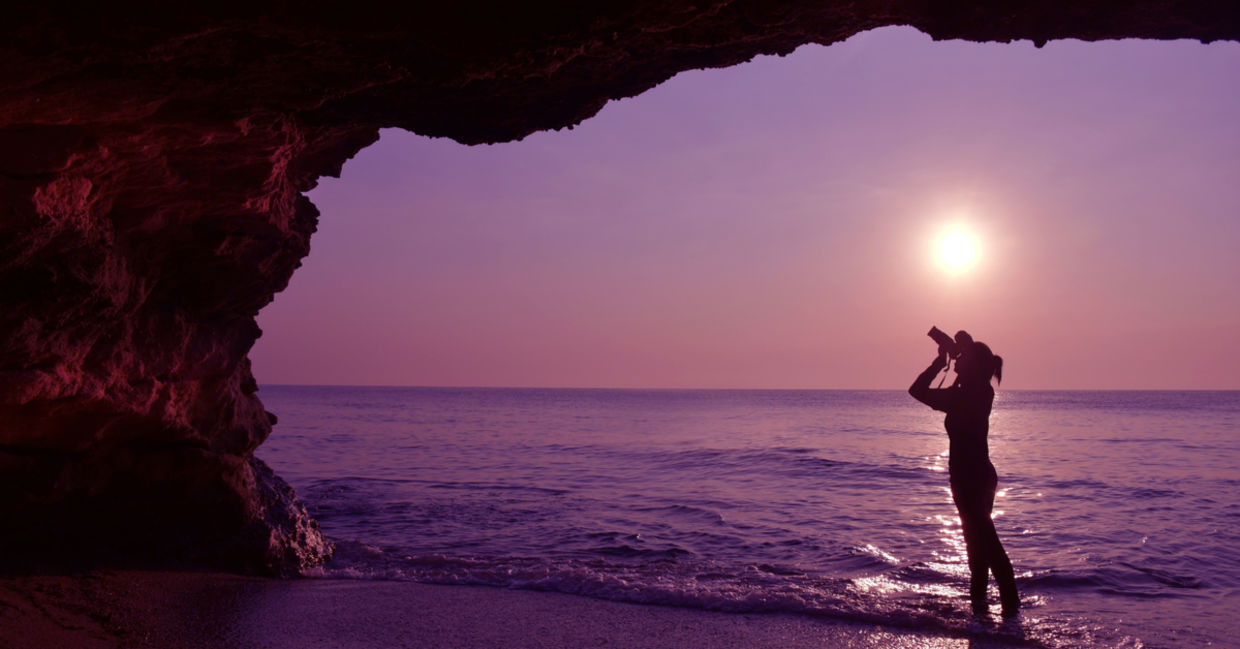 Woman taking a photo in front of a cave at sunrise
