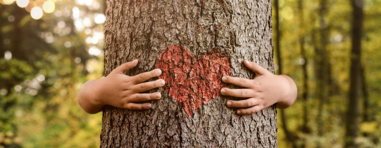A plant empath hugs a tree with a heart painted on the trunk.