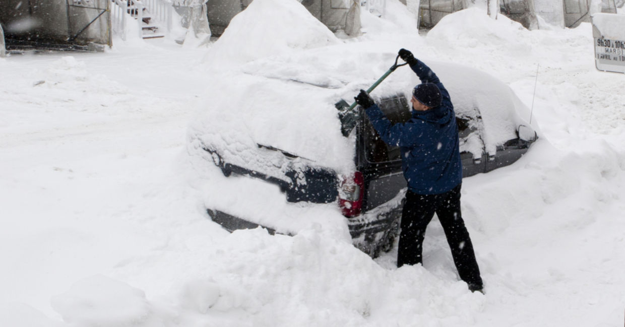 A man uses a shovel to dig his car out of deep snow.
