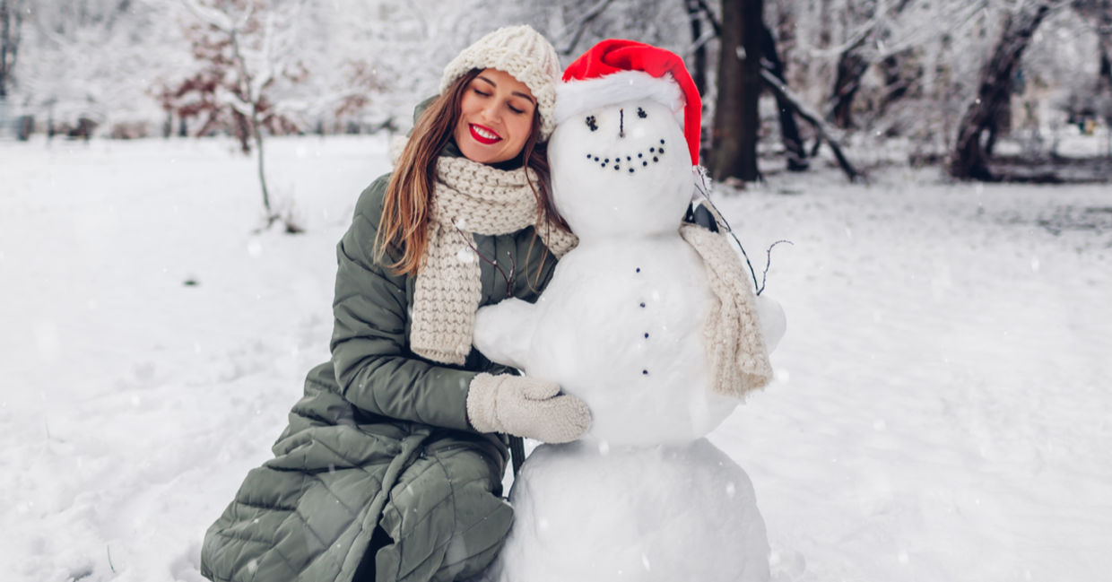 Happy to be outside in the cold winter, a woman hugs a snowman.