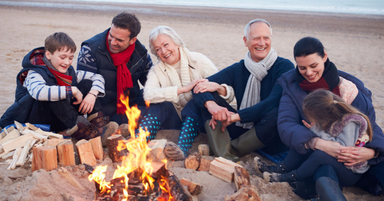 Grandparents, parents, and children connect by enjoying time together around a beach bonfire.