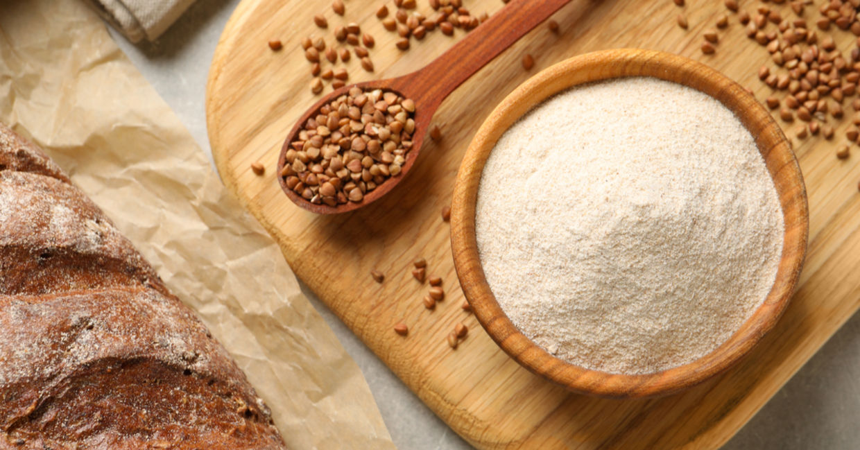 Buckwheat kernels and buckwheat flour beside a freshly baked loaf of gluten-free bread.