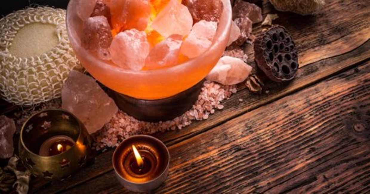 A soothing Himalayan salt lamp, along with tea lights and crystals, are arranged on a wooden surface.