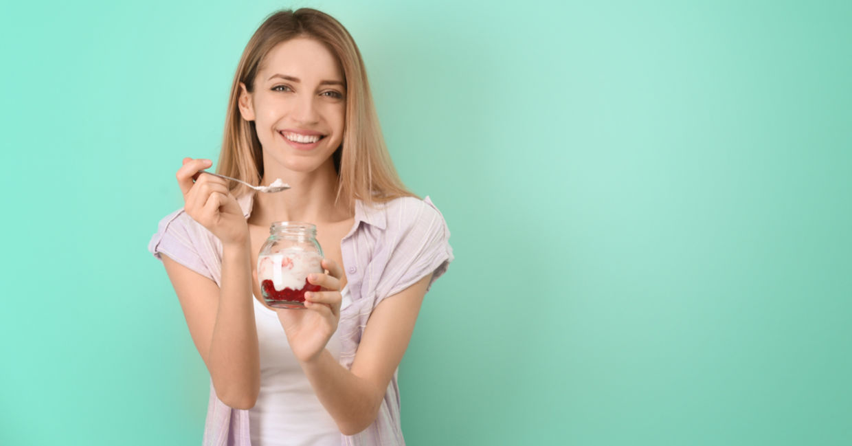 A young woman is eating a gut-healthy breakfast of yogurt with fruit.