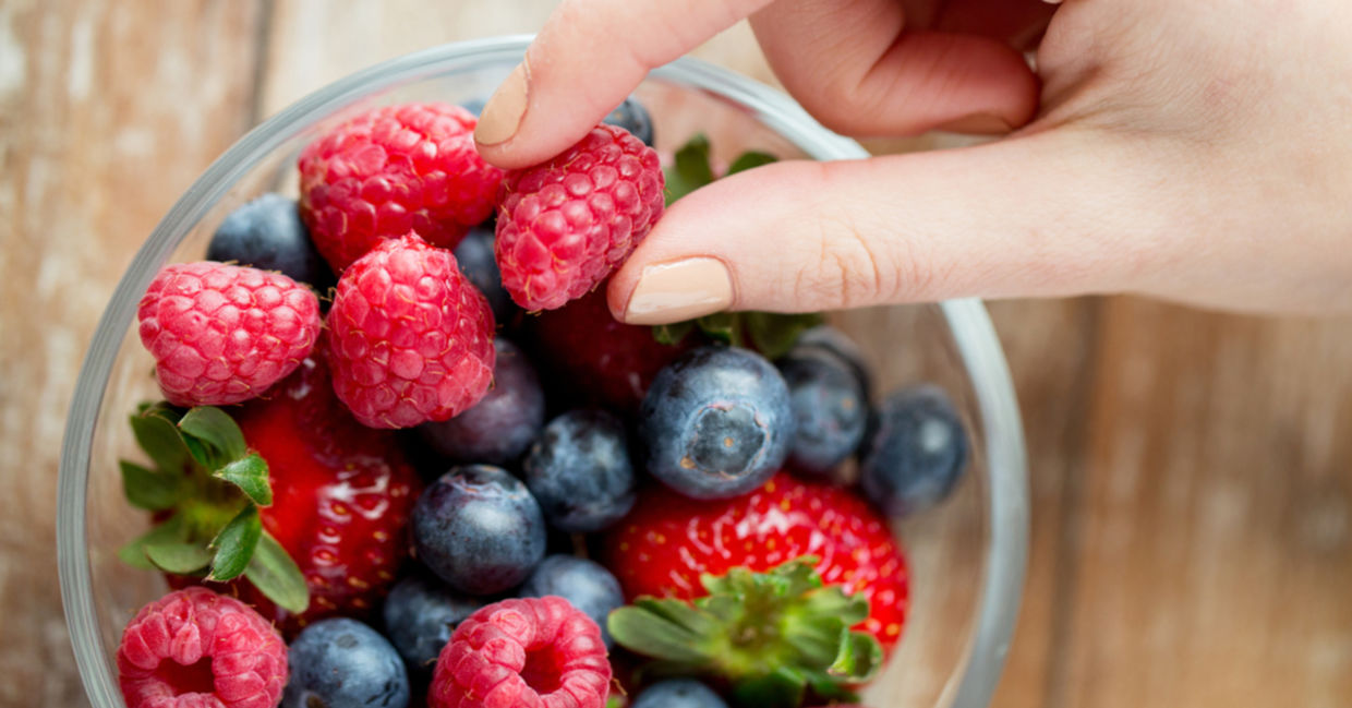 Picking from a bowl of fresh, healthy berries that includes strawberries, raspberries, and blueberries.