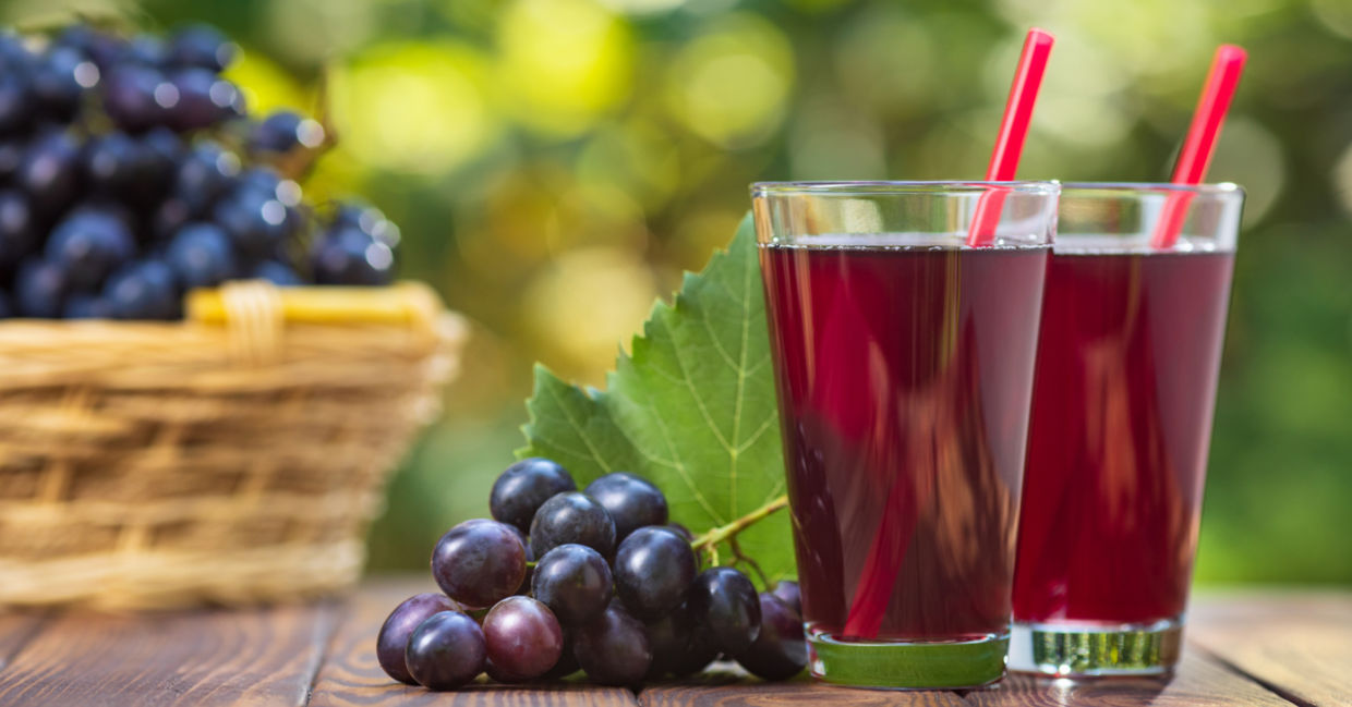 Bunches of purple grapes on a table beside two glasses of fresh grape juice.