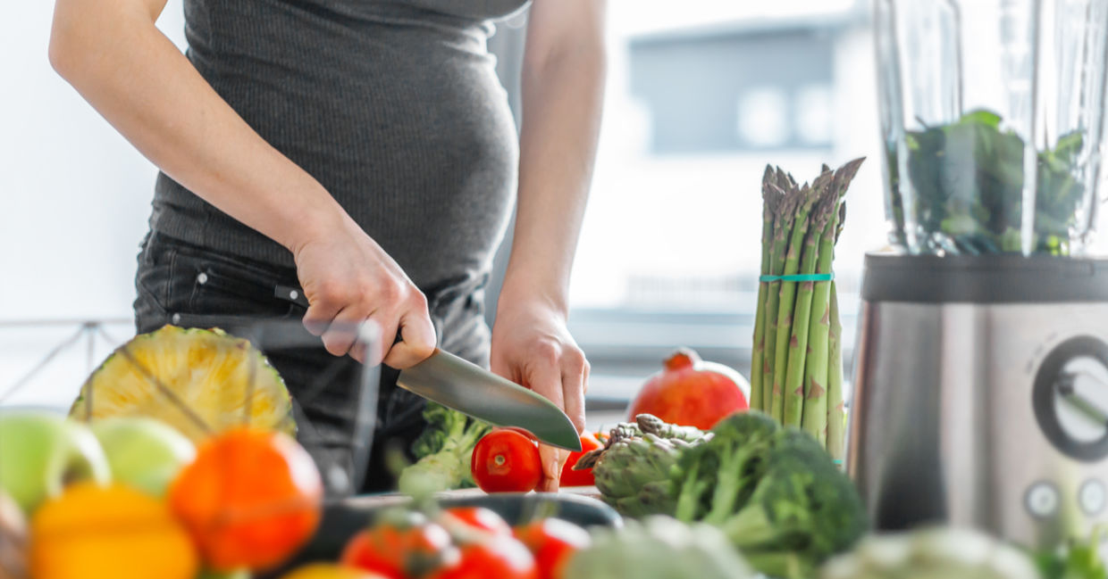 A pregnant woman prepares a healthy meal, including asparagus.