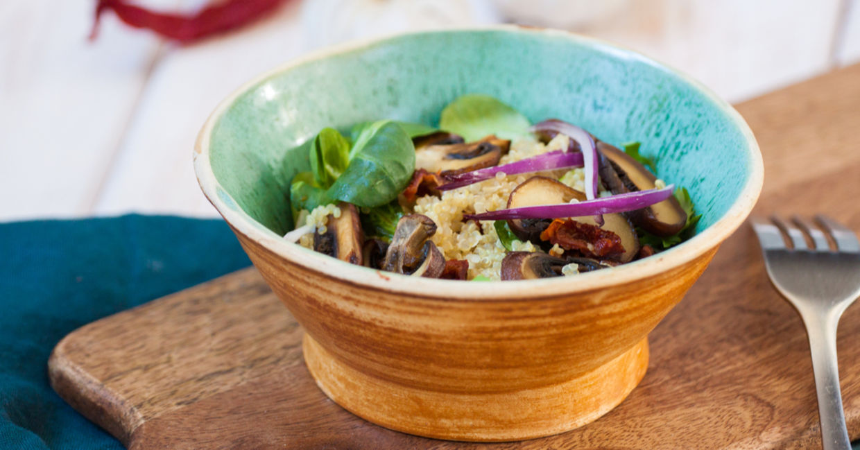 Blue bowl filled with fresh homemade salad with quinoa, spinach and mushrooms.